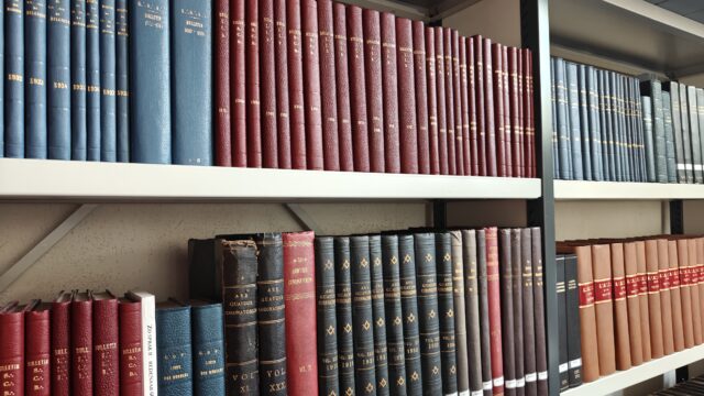 Row of old leather-bound books on a metal library shelf, organized by color (blue, red, teal).1024x768